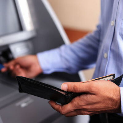 man pulling card out of wallet and inserting it into atm
