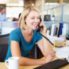 A smiling blonde woman in an office on the telephone