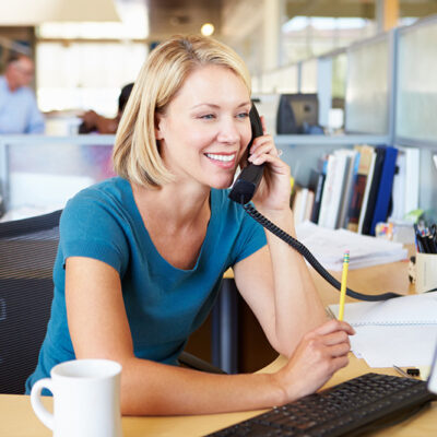 A smiling blonde woman in an office on the telephone