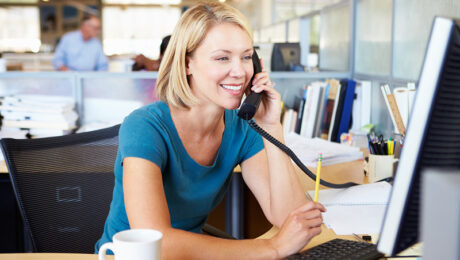 A smiling blonde woman in an office on the telephone